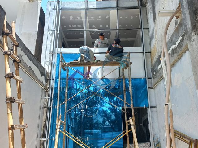 Pemasangan curtain wall fasad kaca gedung warna biru oleh tim CV. Sahrul Aluminium